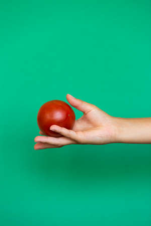 Hand holding a tomato against a yellow backgroundの写真素材