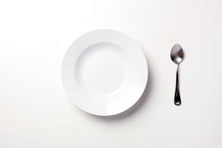 Empty white plate and a spoon on a white table