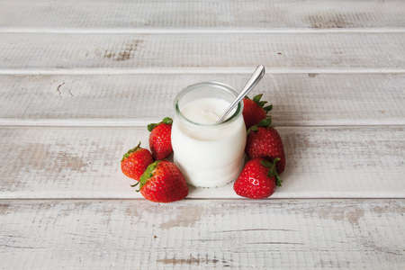 Yogurt in a jar with strawberries on a white wooden tableの写真素材