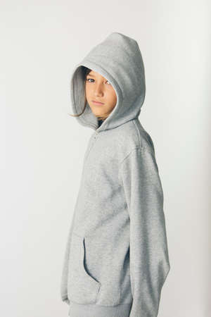 Eleven years old boy with hooded sweater standing against a white backgroundの写真素材