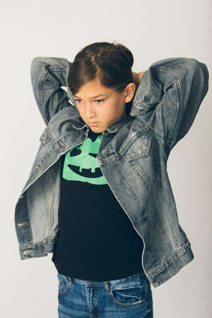 Eleven years old boy with a jean jacket standing against a white backgroundの写真素材