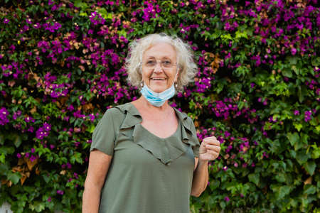Senior woman wearing a blue surgical mask in the streetの写真素材