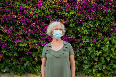 Senior woman wearing a blue surgical mask in the streetの写真素材