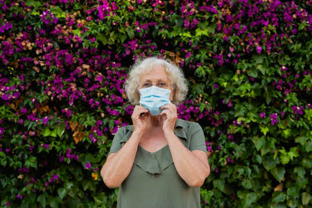 Senior woman wearing a blue surgical mask in the streetの写真素材