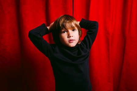 Three years old boy, wearing black clothes, crying against a red curtainの写真素材