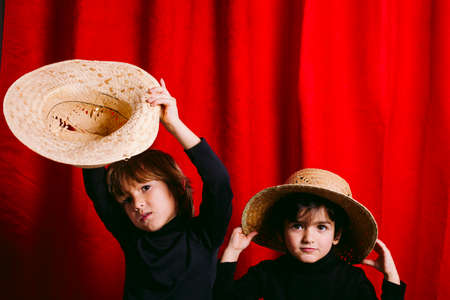 Two boys wearing black clothes and a straw hut, against a red curtainの写真素材