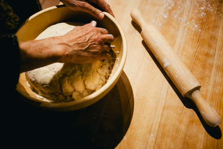 Hands of a woman kneading wheat bread dough on a wooden table