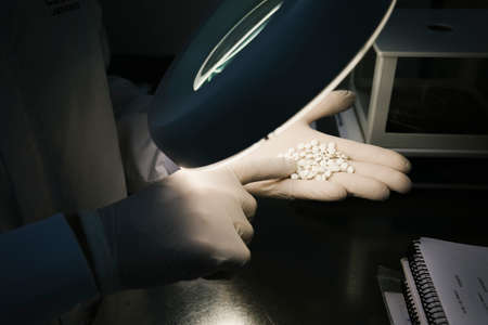 Hands of a scientist examining some white pillsの写真素材