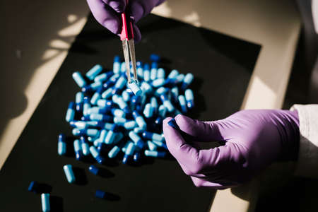 Hands of a scientist working with some blue capsules
