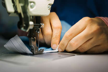 Hands of a seamstress sewing medical clothes with a sewing machine