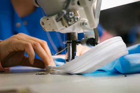 Hands of a seamstress sewing medical clothes with a sewing machine
