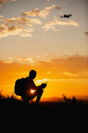 Silhouette of a young man with a backpack operating a drone in A Rural Setting on sunset
