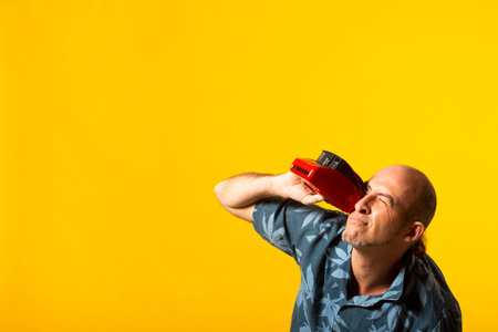 Adult man taking pictures with a red instant camera against a yellow background