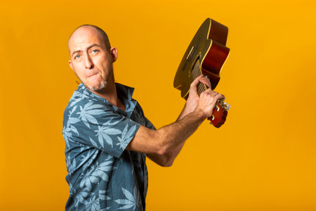 Portrait of an aggressive Musician trying to break his acoustic guitar against a yellow backgroundの写真素材