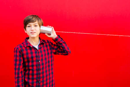 Boy using two metal cans and a thread as a telephone against a red wallの写真素材