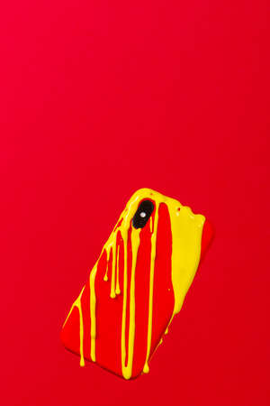 Yellow painting melting on an Smartphone with Red case against a red backgroundの写真素材