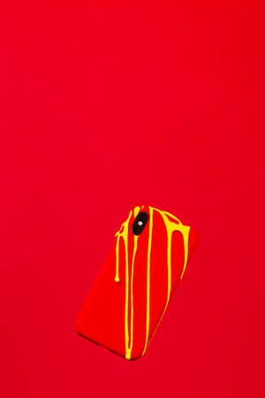 Yellow painting melting on an Smartphone with Red case against a red backgroundの写真素材