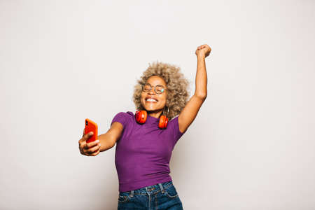 Portrait of Smiling Young woman using smart phone while standing Against White Backgroundの写真素材