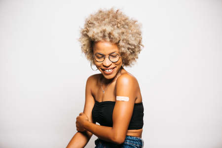 Portrait of a Young black latin woman showing the plaster on her arm after vaccination standing...