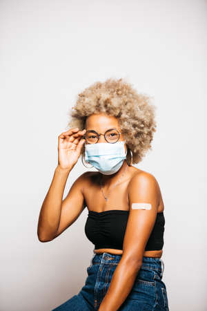 Portrait of a Young black latin woman showing the plaster on her arm after vaccination standing Against White Backgroundの写真素材