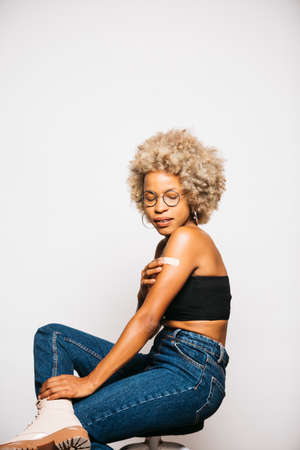 Portrait of a Young black latin woman showing the plaster on her arm after vaccination standing Against White Backgroundの写真素材