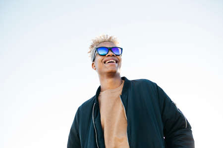Young latin american male with blue sunglasses against a white skyの写真素材