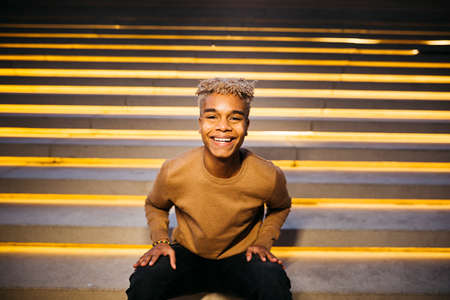 Young latin american male sitting on stairs and smiling at the camera, on the streetの写真素材