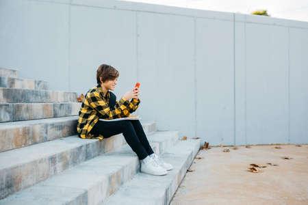 Teenager using a red smartphone and sitting on stairs outdoorsの写真素材