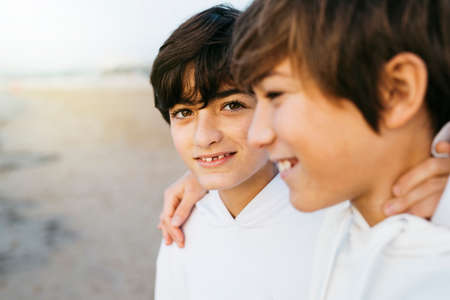 Portrait of two preteen brothers wearing white hooded sweater on the beach, on winterの写真素材