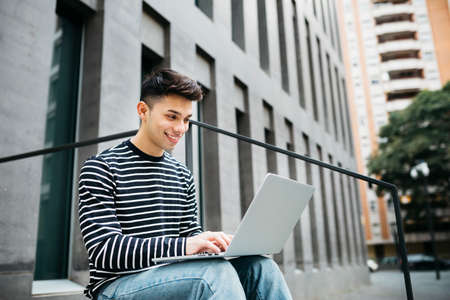 Young man, sitting on street stairs, using a laptopの写真素材