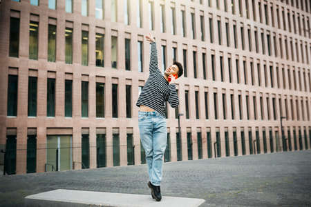 Young man talking on a red smartphone while dancing on a street benchの写真素材