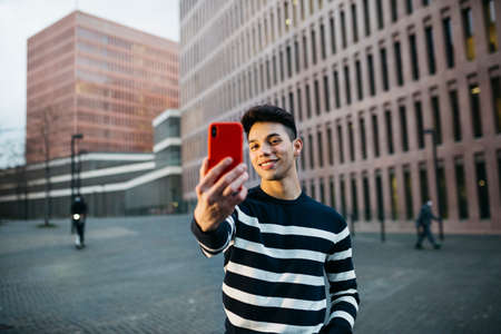 Young smiling man taking a selfie on a red smartphone the a streetの写真素材