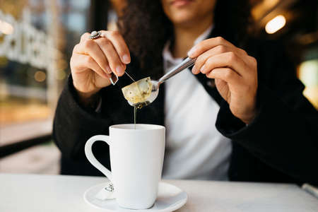 Close up of young woman's hands with a white mug preparing tea in a coffeeshop