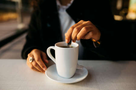 Close up of young woman's hands with a white mug preparing tea in a coffeeshop