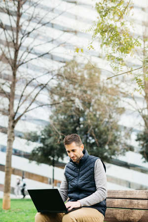 Freelancer male in casual clothes, using smartphone, modern building on background. Working remotely...