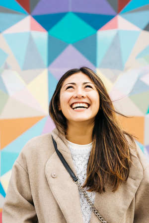 Portrait of a young smiling woman against a colorful graffitiの写真素材