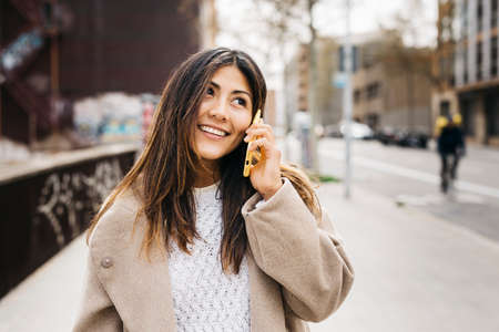 Portrait of a young smiling woman talking on a phone in the streetの写真素材