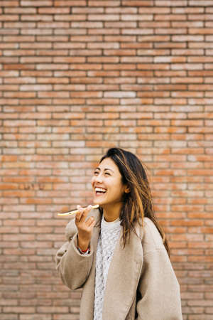Portrait of a young woman, using a phone, against a brick wallの写真素材