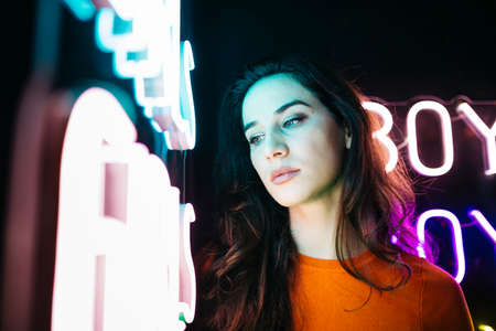 Portrait of brunette caucasian girl with long hair, next to a colorful neon light