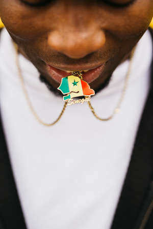 Close up of a Senegal shaped medal with its flag on it held by a black male with his mouth