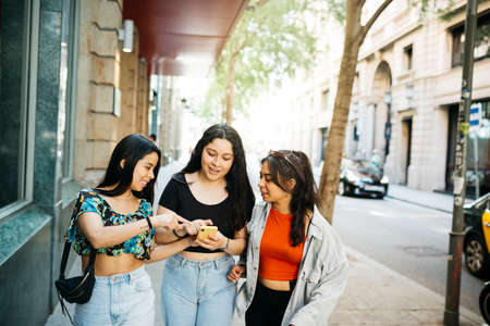 Three young women walking and hanging out on a commercial street of a big cityの写真素材