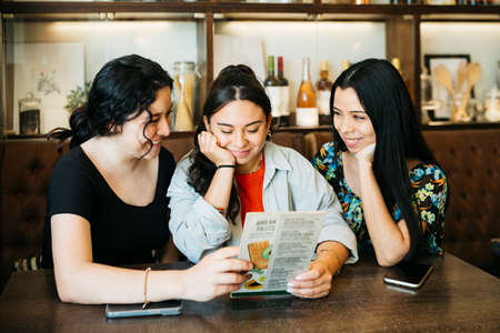 Three young women looking at a menu in a restaurantの写真素材
