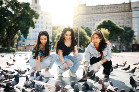 Three young women feeding pigeons in a square of a city