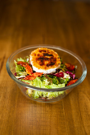 Green salad with cheese on top in a big bowl on a wooden tableの写真素材