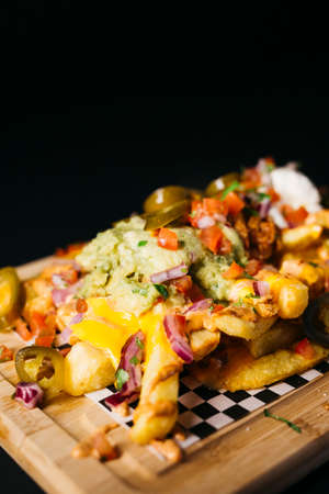 Fried potatoes topped with melted cheese and other savory toppings over a black backgroundの写真素材