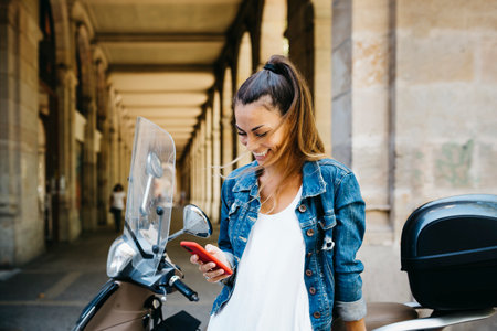Young smiling woman on a motorbike using on a red smartphoneの写真素材