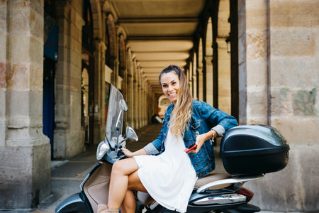 Young smiling woman sitting on a motorbike using on a red smartphoneの写真素材