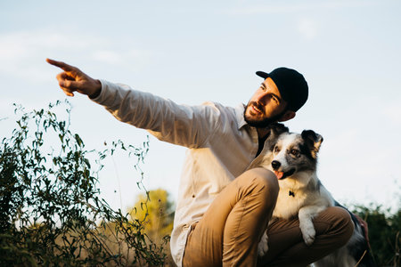 Portrait of a young bearded man wearing a black cap, with his dog, at countrysideの写真素材