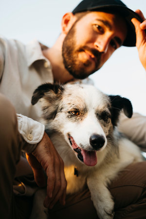 Portrait of a young bearded man wearing a black cap, with his dog, at countrysideの写真素材