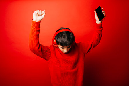 Pre-adolescent boy wearing a red sweater and red headphones over a red background, listening to music and dancingの写真素材